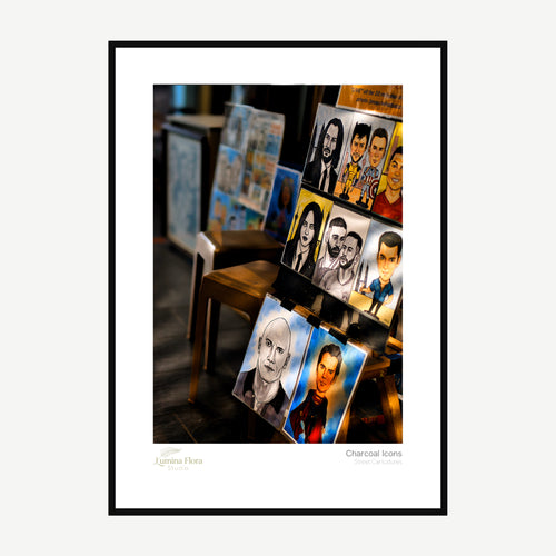 Framed print: charcoal caricature drawings displayed on street easels, black wood frame