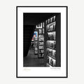Framed print: dim bookshop interior with shelves and stairs in selective colour, black wood frame
