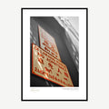 Framed print: multilingual warning sign with red text on a grey wall, black wood frame